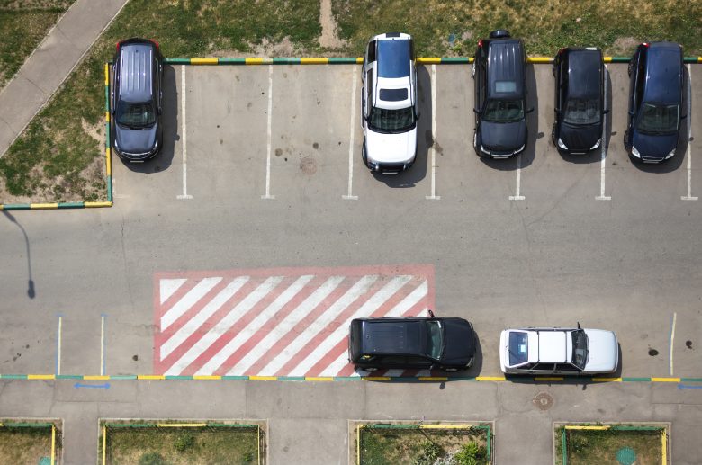 A parking lot shows several cars backed into parking spaces