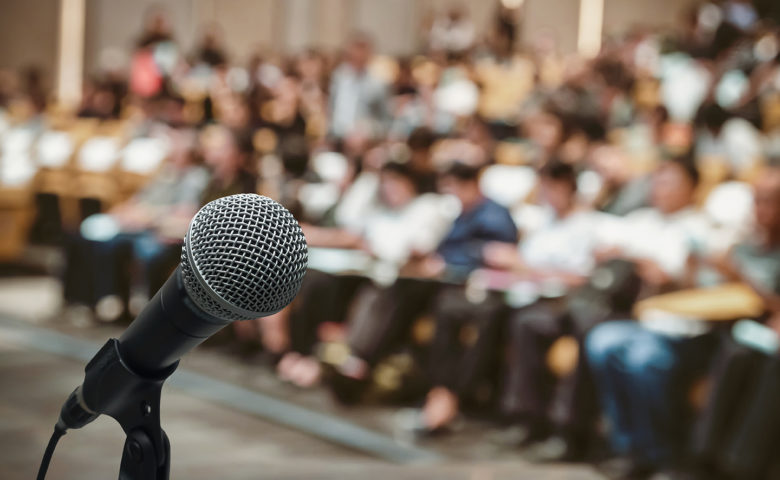 Microphone with blurred photo of conference hall with attendees background