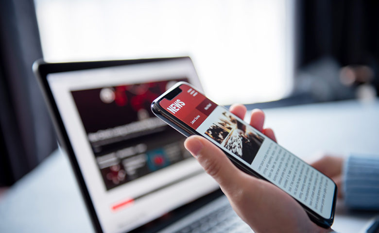 Online news on a smartphone and laptop, Woman reading news or articles in a mobile phone screen application at home. Newspaper and portal on internet.