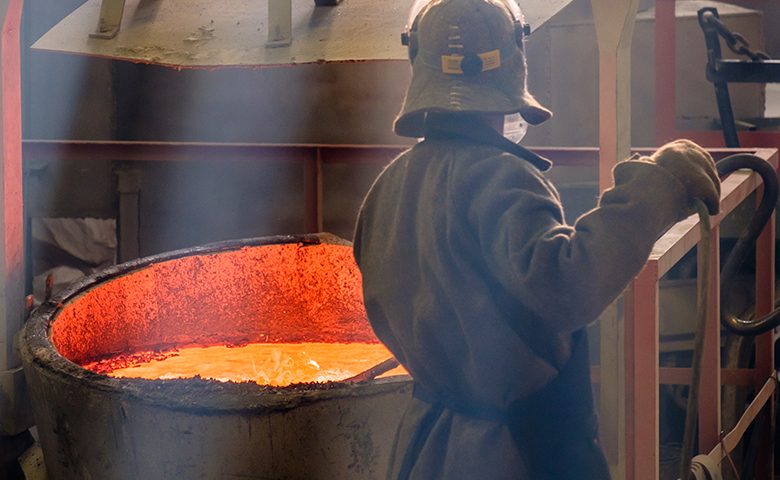 a worker with a metal pole at a vat of molten red metal