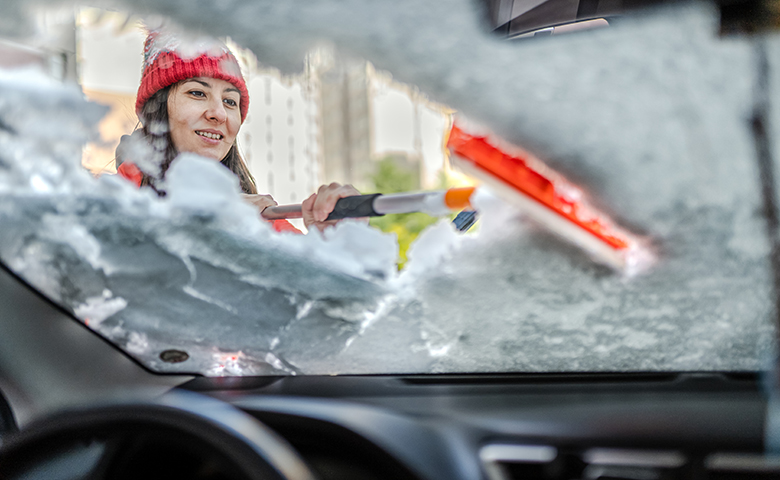 Woman in winter jacket scraping ice and snow from car windows