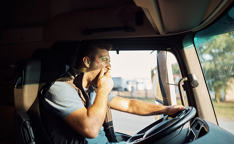 Tired truck driver yawning behind the steering wheel.